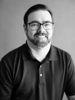 Black and white portrait of appraiser Josh Ament, smiling, wearing glasses